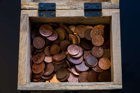 on the picture you can see a small wooden treasure chest in which you can see many different coins.の写真素材
