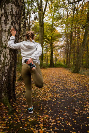 A girl who stretch her right leg next to a tree in the forrestの写真素材