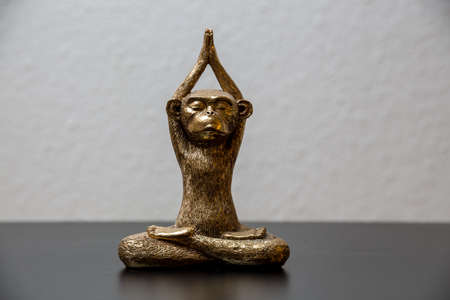 A gold colored meditating monkey statue sitting on a black surface, the background of the picture is white and blurry.の写真素材