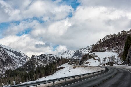 Winter road trough snowcaped mountains in eastern norway, With a cloudy blue skyの写真素材