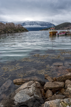 View over Norwegian fjord, With small fishing boat by small wooden pierの写真素材
