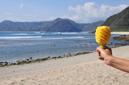 carved pineapple in hand at beachの写真素材