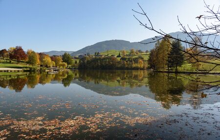 View of Lake Ritzensee on a sunny autumn day in Saalfelden with still reflecting water mountain with clear blue sky. Saalfelden, Pinzgau, Salzburg Land, Austria, Europe.の写真素材