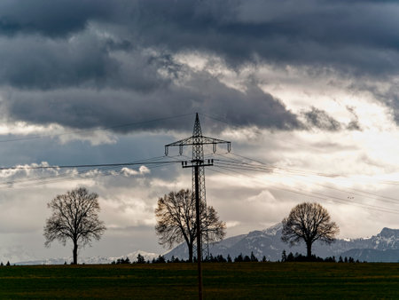 Low angle view of electricity pylon on field against cloudy skyの写真素材