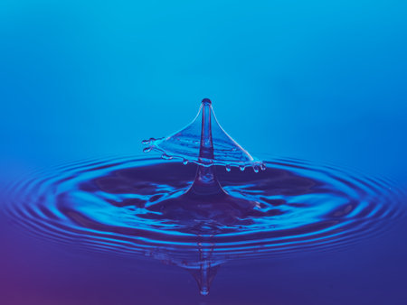 Water drop collision on a blue background. Splash effect after collision a falling drops with water surfaceの写真素材