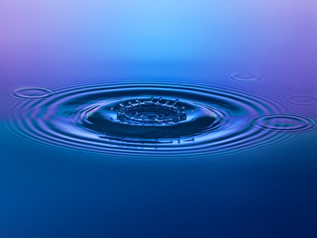 Water drop falling into water with ripples and ripples on blue backgroundの写真素材