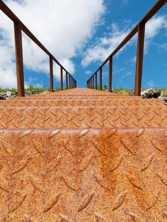 Old rusty metal stairs with blue sky and white clouds in the backgroundの写真素材