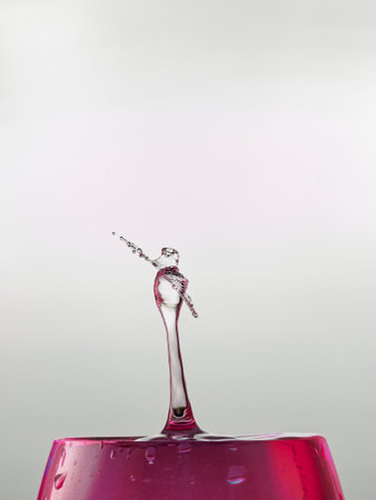water drop collision on a wet glass of red wine with gray background
