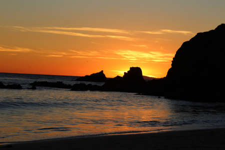 Sunset over the ocean and rock jetty at Shaws Cove in Laguna Beach Southern Californiaの写真素材