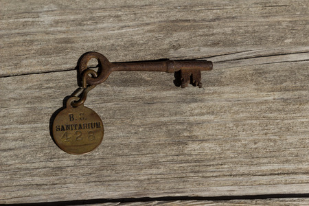 Old rusty skeleton key to a sanitarium  mental hospital on a wood benchの写真素材