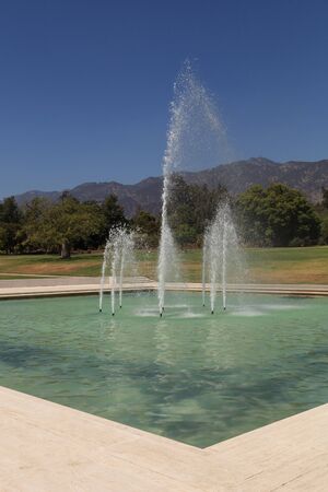 Blue spraying fountain of water with the mountains in the background in gardens in California, United Statesの写真素材