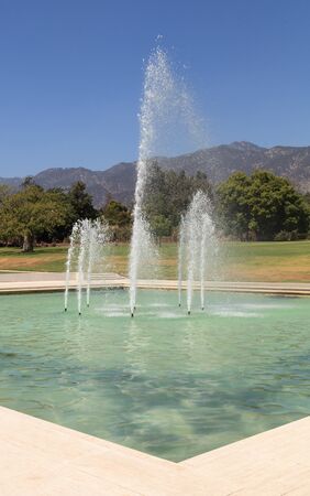 Blue spraying fountain of water with the mountains in the background in gardens in California, United Statesの写真素材