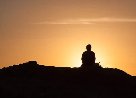 Silhouette of lone man sitting on a rock near the sea and watching the sunsetの写真素材