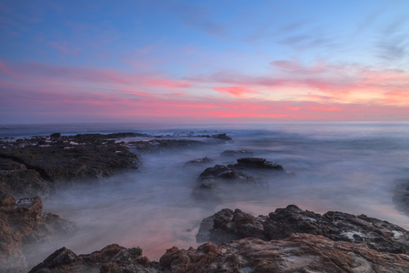 Long exposure of sunset over rocks, giving a mist like effect over ocean in Laguna Beach, California, United Statesの写真素材