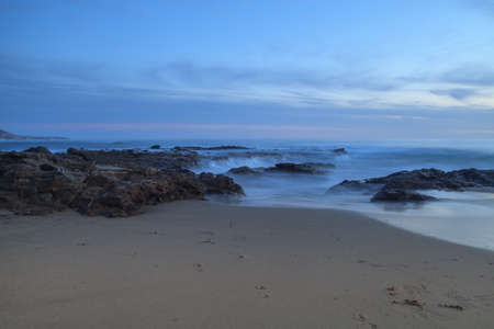 Long exposure of sunset over rocks, giving a mist like effect over ocean in Laguna Beach,...
