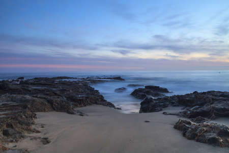 Long exposure of sunset over rocks, giving a mist like effect over ocean in Laguna Beach, California, United Statesの写真素材