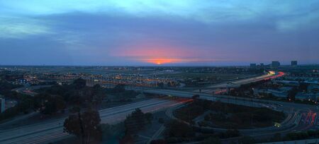 Aerial view of John Wayne Airport in Orange County, California, at sunset with rain in the air light trails across the 405 highway in front.のeditorial素材