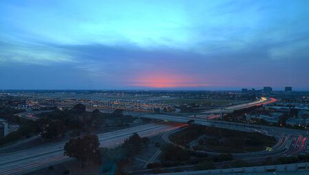 Aerial view of John Wayne Airport in Orange County, California, at sunset with rain in the air light trails across the 405 highway in front.のeditorial素材