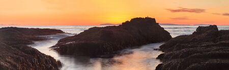 Long exposure of sunset over rocks, giving a mist like effect over ocean in Laguna Beach, California, United Statesの写真素材