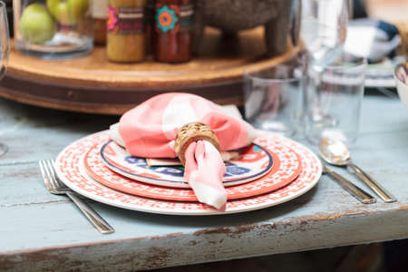Rustic farm place setting with white and red plates, napkins and clear wine glasses on a distressed...