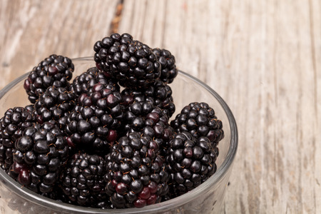 Clear glass bowl of ripe blackberries on a rustic farm picnic table in summer.