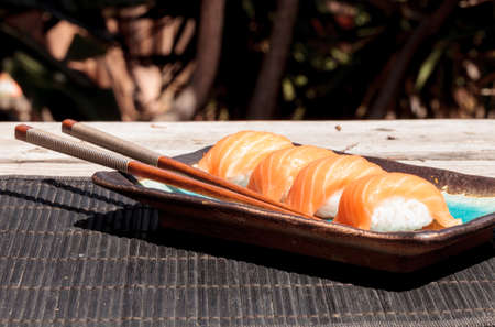 A meal of salmon sushi on white rice on a blue plate with chopsticks.の写真素材