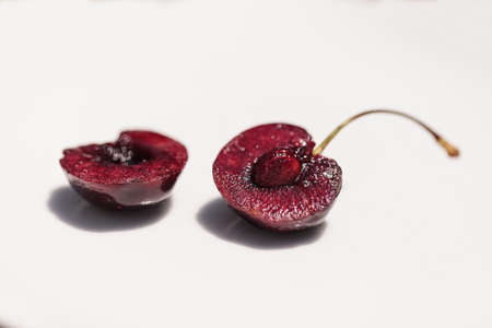 Macro of a dark red black cherry with a green stem on a white background.の写真素材