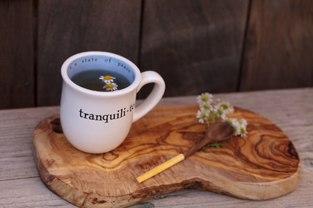 Chamomile tea with chamomile daisy flowers in a hot white cup on a wooden rustic cutting board and a spoon. This home remedy is known to help sleep and aid a sore throatの写真素材