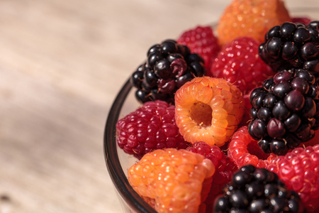 Organic golden and red raspberries mixed with blackberries in a glass bowl on a rustic farm table.