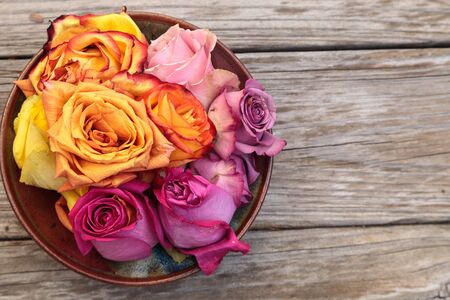 Rose petals in a bowl in the colors of a sunset, including orange, yellow, pink and purple