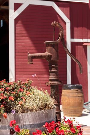 Well water pump on a farm in summer with flowers and a barnの写真素材