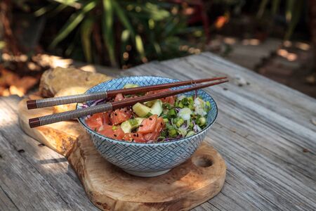 Raw salmon poke bowl with rice, cabbage, cucumber, sesame seeds and spring rolls with chopsticks.の写真素材