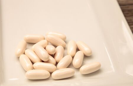 White gel capsules of vitamin Co Q-10 also called coenzyme q10 displayed on a white surface.