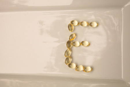 Gold gel capsule of vitamin E displayed on a white surface.の写真素材