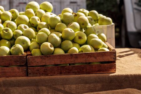 Bushel of green apples in a crate at a farmerâs market with other fruits and vegetables.の写真素材