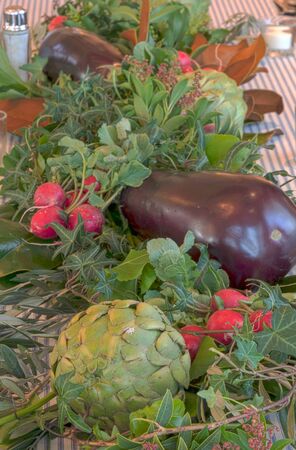 Table decor background of purple eggplant, red radish bushels, and green artichokes on a country farm table.の写真素材