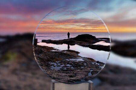 Lone man through a crystal ball on the rocks at sunset at Treasure Island Beach in Laguna Beach, California, United Statesの写真素材