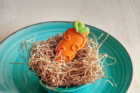 Orange carrot sugar cookie in an Easter basket nest during the religious holiday.