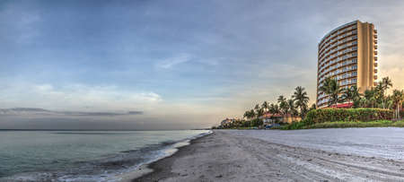 Vanderbilt Beach at sunrise with a calm ocean and buildings along the white sand in Naples, Florida.のeditorial素材