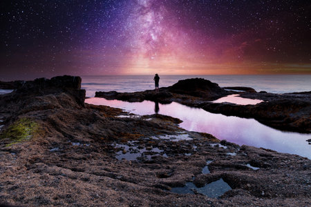 Night stars over Manâ€™s reflection silhouette at the ocean water as it cascades over rocks in...