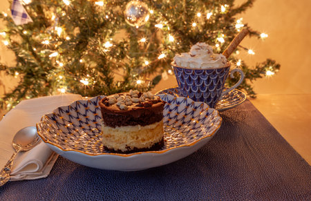 Hot chocolate and layered dark and white chocolate dessert on a fancy bone China plate tipped with gold and a silver spoon in front of a Christmas tree.の写真素材