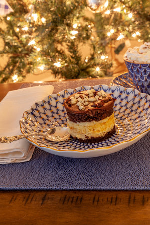 Hot chocolate and layered dark and white chocolate dessert on a fancy bone China plate tipped with gold and a silver spoon in front of a Christmas tree.の写真素材