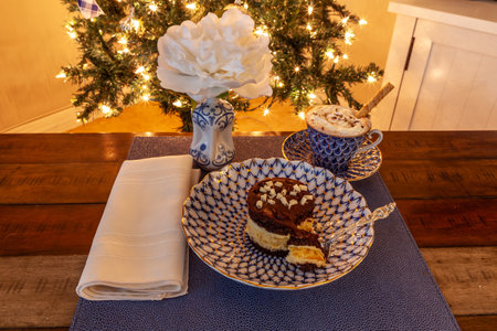 Hot chocolate and layered dark and white chocolate dessert on a fancy bone China plate tipped with gold and a silver spoon in front of a Christmas tree.の写真素材