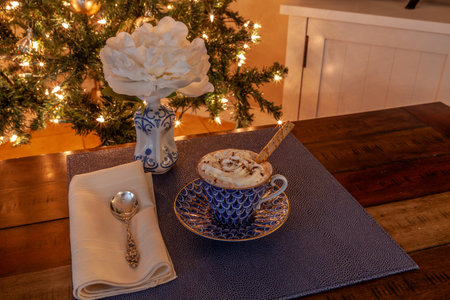 Hot chocolate and layered dark and white chocolate dessert on a fancy bone China plate tipped with gold and a silver spoon in front of a Christmas tree.の写真素材