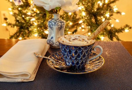 Cup of Hot chocolate in a fancy bone China cup with gold and a silver spoon in front of a Christmas tree.の写真素材