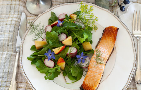 Organic greens salad with purple borage flowers, arugula, radish and salmon on a fine China dish with elegant silverware.の写真素材