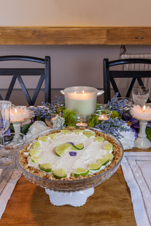 Key lime Cheesecake on an antique cake stand on a table set with candles and flowers.