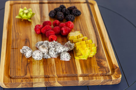 Wood cutting board with fruit including dragon fruit, star fruit, raspberries, blackberries, and kiwi.の写真素材