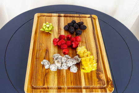 Wood cutting board with fruit including dragon fruit, raspberries, blackberries, and kiwi.の写真素材