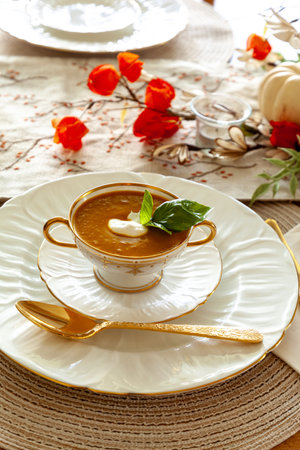 Orange pumpkin and ginger soup served on gold rimmed white plates with autumn table setting.の写真素材